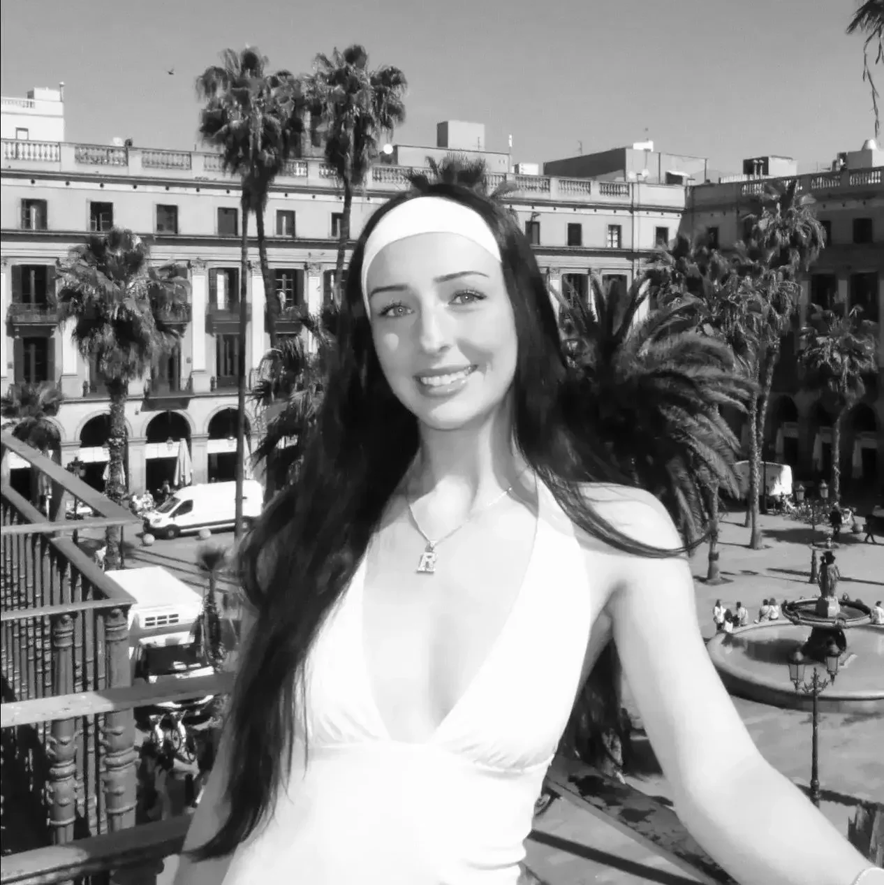 a woman smiling while standing outdoors in a plaza, surrounded by palm trees and historical buildings. the image is in black and white. at floka hair salon on bayview in toronto